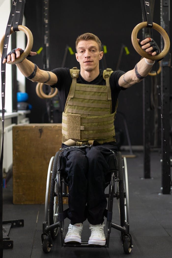 A focused athlete in a wheelchair performs exercises with gymnastic rings indoors, showcasing strength and determination.